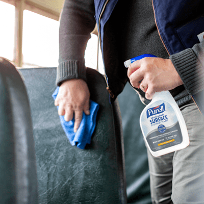A person using PURELL Surface spray to wipe down a school bus seat